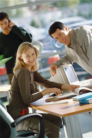 simsearch:695-03374588,k - Office scene, man leaning toward female colleague, both smiling at camera Stock Photo - Premium Royalty-Free, Code: 695-03374594