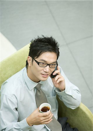 Businessman sitting in armchair, using cell phone and holding cup of coffee Stock Photo - Premium Royalty-Free, Code: 695-03374702