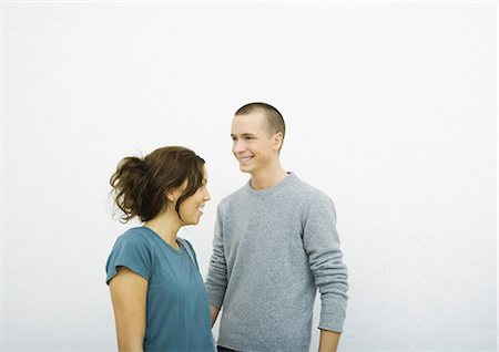 simsearch:632-01277233,k - Young man and young woman standing together, looking in opposite directions, smiling Fotografie stock - Premium Royalty-Free, Codice: 695-03374776