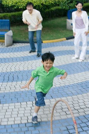 father being chased by kids - Boy chasing hoop, parents watching Stock Photo - Premium Royalty-Free, Code: 695-03374919