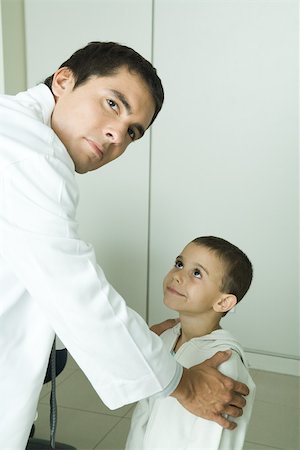 paediatrician (male) - Boy looking up at doctor, doctor holding boy by shoulders, looking over shoulder at camera Stock Photo - Premium Royalty-Free, Code: 695-03375268