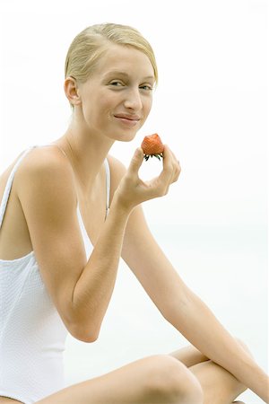 Teenage girl wearing bathing suit, holding up strawberry, smiling Stock Photo - Premium Royalty-Free, Code: 695-03375414