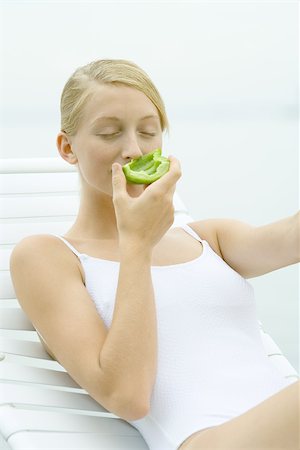simsearch:695-03375411,k - Teenage girl wearing bathing suit, sitting in lounge chair, smelling piece of green pepper Stock Photo - Premium Royalty-Free, Code: 695-03375425