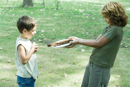 Boy handing friend plate of grilled meat Stock Photo - Premium Royalty-Free, Code: 695-03375472