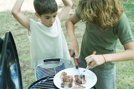 Boy cutting up meat on plate while second boy watches Stock Photo - Premium Royalty-Free, Code: 695-03375480
