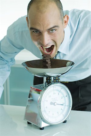 simsearch:695-03375576,k - Man leaning toward stack of chocolate chunks on kitchen scale with mouth wide open Foto de stock - Sin royalties Premium, Código: 695-03375547