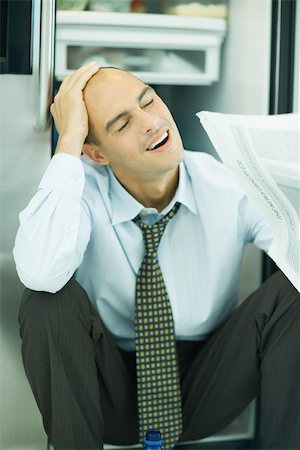 simsearch:632-05604352,k - Man sitting in front of open refrigerator, hand on head, eyes closed, holding newspaper Stock Photo - Premium Royalty-Free, Code: 695-03375555