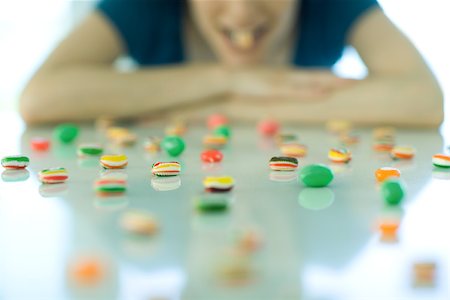 simsearch:695-03375576,k - Table spread with candy, woman resting head on arms, holding piece of candy between teeth Foto de stock - Sin royalties Premium, Código: 695-03375571