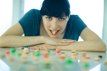 simsearch:695-05779160,k - Table spread with candy, woman resting head on arms, holding piece of candy between teeth Stock Photo - Premium Royalty-Free, Code: 695-03375572