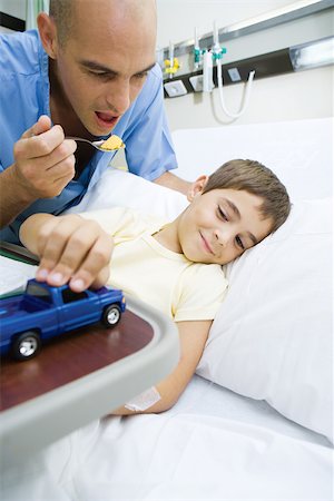 Boy lying in hospital bed, doctor encouraging boy to eat meal Foto de stock - Sin royalties Premium, Código: 695-03375863