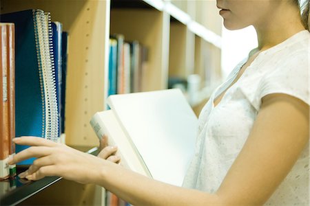 simsearch:632-01380739,k - Jeune femme à atteindre pour les livres sur une étagère de bibliothèque, recadrée vue Photographie de stock - Premium Libres de Droits, Code: 695-03376129