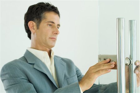 Man in suit inspecting lock on door Stock Photo - Premium Royalty-Free, Code: 695-03376197