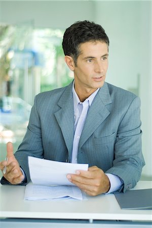 Mature businessman sitting at desk, holding document and speaking Stock Photo - Premium Royalty-Free, Code: 695-03376193