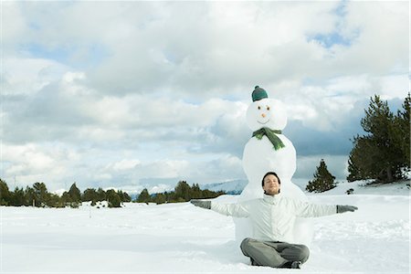 snow cone - Jeune homme assis sur le sol devant le bonhomme de neige, souriant, bras tendus Photographie de stock - Premium Libres de Droits, Code: 695-03376328