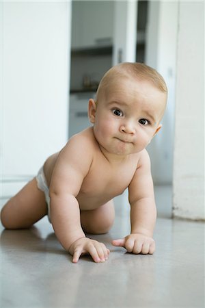 Baby crawling on floor, biting lip, looking at camera, full length Stock Photo - Premium Royalty-Free, Code: 695-03376598
