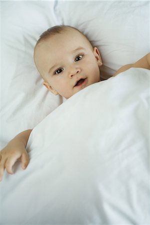 Baby in bed under duvet, looking at camera, high angle view Foto de stock - Sin royalties Premium, Código: 695-03376614
