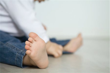 Baby wearing jeans, sitting on floor, low section, focus on foreground Stock Photo - Premium Royalty-Free, Code: 695-03376628