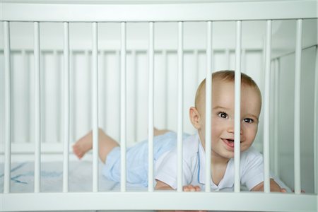 Baby lying on stomach, looking through bars of crib, smiling Stock Photo - Premium Royalty-Free, Code: 695-03376639