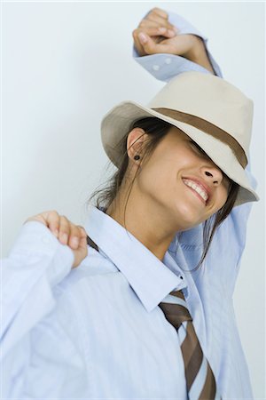 Teenage girl wearing tie and hat, smiling at camera, arms raised, portrait Stock Photo - Premium Royalty-Free, Code: 695-03376678