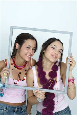 simsearch:696-03394580,k - Two young female friends holding up picture frame, smiling at camera, portrait Stock Photo - Premium Royalty-Free, Code: 695-03376837