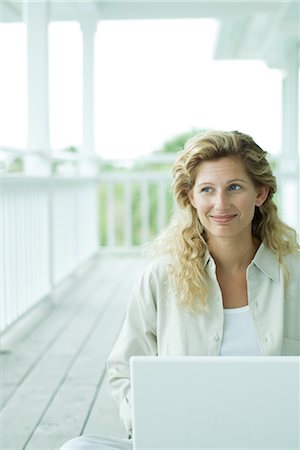 simsearch:695-03377942,k - Woman sitting on porch, using laptop computer, looking away, smiling Foto de stock - Royalty Free Premium, Número: 695-03376934