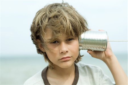 Boy holding tin can phone up to ear, looking at camera, portrait Stock Photo - Premium Royalty-Free, Code: 695-03376938