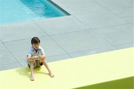 Boy sitting on the ground by swimming pool, looking at cell phone Stock Photo - Premium Royalty-Free, Code: 695-03376942