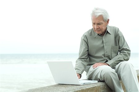 Senior man sitting outdoors using laptop computer, looking down Stock Photo - Premium Royalty-Free, Code: 695-03376955