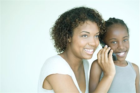 simsearch:632-01271195,k - Mother holding cell phone up to daughter's ear, both smiling, daughter looking at camera Fotografie stock - Premium Royalty-Free, Codice: 695-03376953