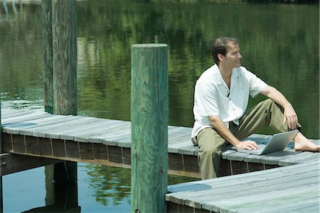 Man sitting on dock, using laptop computer, looking away Stock Photo - Premium Royalty-Free, Code: 695-03376964