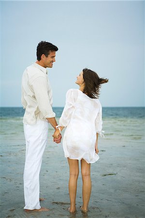 simsearch:695-05767093,k - Man and young female companion on beach, holding hands, looking at each other, full length Fotografie stock - Premium Royalty-Free, Codice: 695-03376997