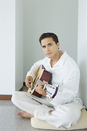 Young man sitting on cushion playing acoustic guitar, looking at camera Stock Photo - Premium Royalty-Free, Code: 695-03377142