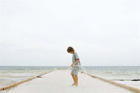 Boy standing on pier holding plastic hoop, looking down, side view Stock Photo - Premium Royalty-Free, Code: 695-03377167