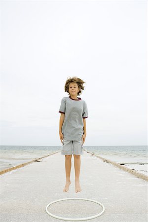 Boy jumping over plastic hoop at the beach, smiling at camera Stock Photo - Premium Royalty-Free, Code: 695-03377169