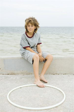 Boy sitting on low wall at the beach, foot touching plastic hoop Stock Photo - Premium Royalty-Free, Code: 695-03377174