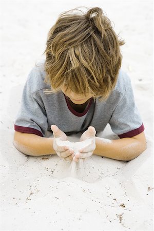 Boy lying on the ground, looking down at handful of sand Stock Photo - Premium Royalty-Free, Code: 695-03377190