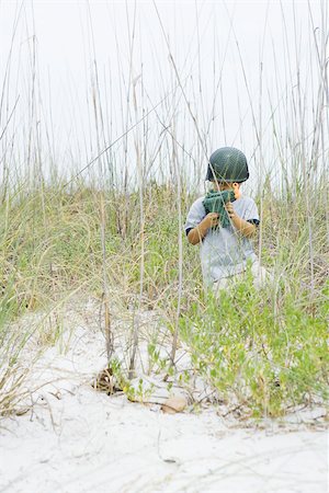 Boy crouching in tall grass, holding toy gun, looking at camera Stock Photo - Premium Royalty-Free, Code: 695-03377211