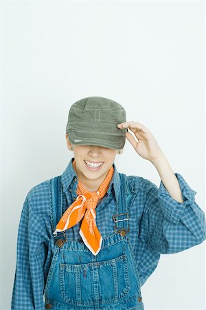 saudando - Teenage girl dressed in overalls, hat covering eyes, smiling Foto de stock - Royalty Free Premium, Número: 695-03377342
