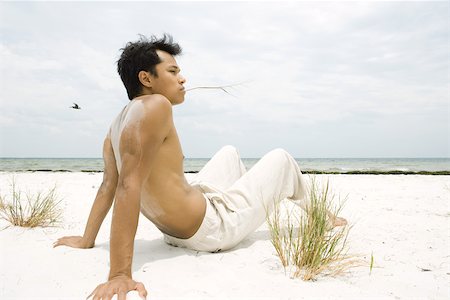 pelecanus - Barechested man sitting on beach, holding blade of grass in mouth, full length Foto de stock - Sin royalties Premium, Código: 695-03377555