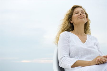 simsearch:633-03444734,k - Woman sitting with eyes closed, smiling, sky in background, low angle view Stock Photo - Premium Royalty-Free, Code: 695-03377584