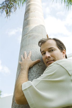 Man embracing tree, looking over shoulder at camera, low angle view Stock Photo - Premium Royalty-Free, Code: 695-03377736