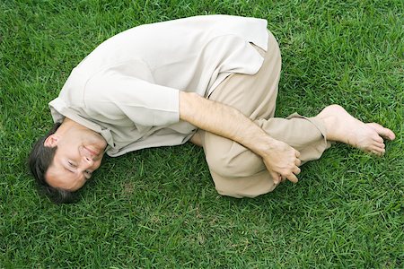 Man lying in fetal position on grass, smiling up at camera Stock Photo - Premium Royalty-Free, Code: 695-03377745