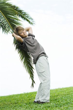 simsearch:695-03377755,k - Boy leaning against palm branch, smiling at camera Stock Photo - Premium Royalty-Free, Code: 695-03377756