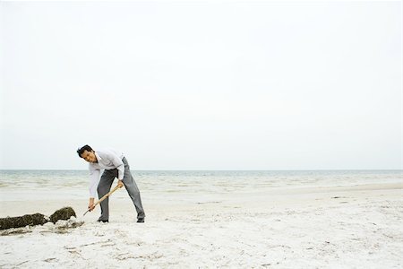 Man at the beach, bending over and digging in sand, smiling at camera Stock Photo - Premium Royalty-Free, Code: 695-03377765