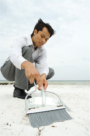 simsearch:632-01828543,k - Man crouching on beach, sweeping sand into dustpan, low angle view Foto de stock - Royalty Free Premium, Número: 695-03377763