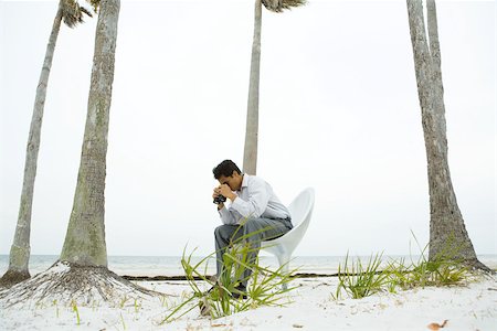 Man sitting in chair at the beach, looking at ground through binoculars Stock Photo - Premium Royalty-Free, Code: 695-03377775