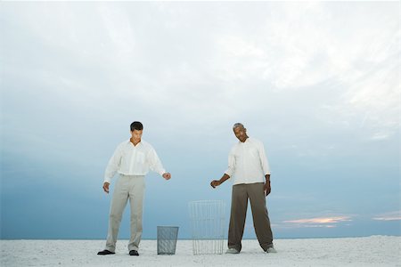 Two men at the beach holding their hands over garbage cans, one looking at camera Stock Photo - Premium Royalty-Free, Code: 695-03377796