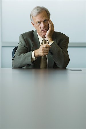 Businessman sitting with hand under chin, holding glasses in hand, looking at camera Stock Photo - Premium Royalty-Free, Code: 695-03377826