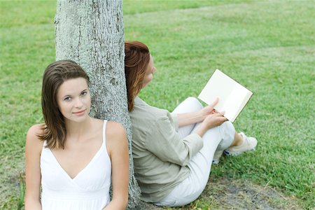 simsearch:695-03377942,k - Mother and daughter leaning against tree trunk, woman reading book, teen girl smiling at camera Foto de stock - Royalty Free Premium, Número: 695-03377924