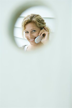 framing face - Woman using cell phone, smiling at camera, viewed through hole Stock Photo - Premium Royalty-Free, Code: 695-03377950